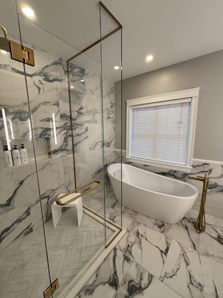 Luxurious bathroom with marble walls, a freestanding bathtub, and a glass-enclosed shower in custom home renovation.